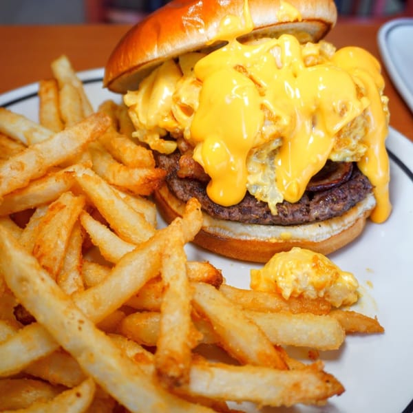 A Pantano's Eatery burger with melted cheese and scrambled eggs, served with a side of fries.
