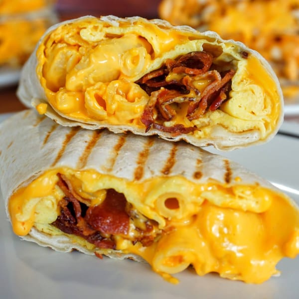 A grilled breakfast burrito, cut in half, revealing scrambled eggs, bacon, and mac and cheese.