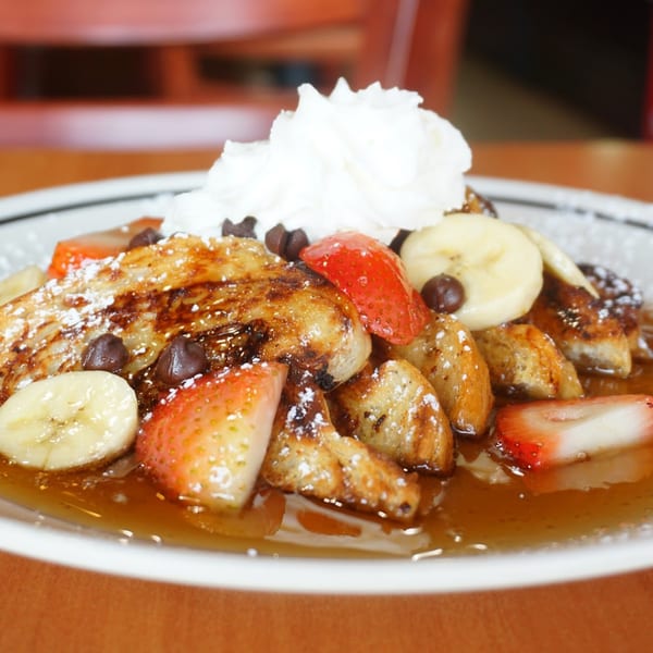 French toast bites with strawberries, bananas, chocolate chips, whipped cream, and syrup.
