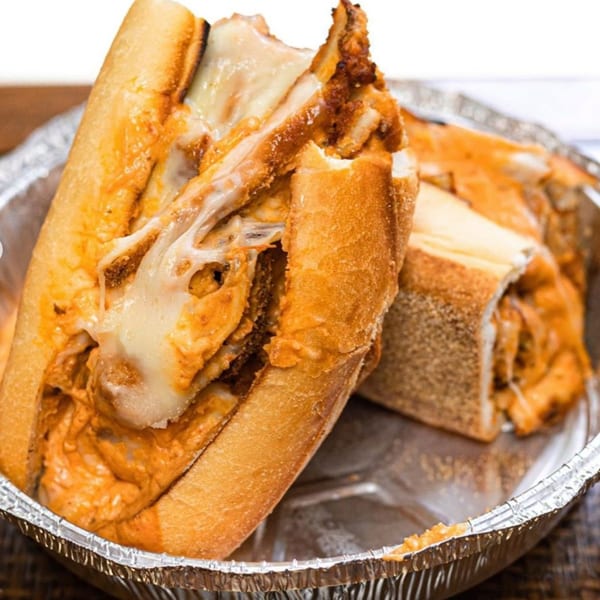 Two halves of a cheesy chicken sandwich in a foil container from Pantano's Eatery.