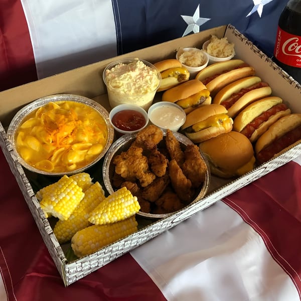 A catering box with hot dogs, cheeseburger sliders, mac and cheese, corn, chicken tenders, and sides.