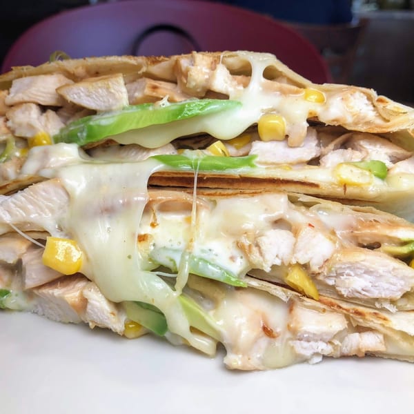 Close-up of a chicken quesadilla with melted cheese, corn, and avocado slices on a white plate.