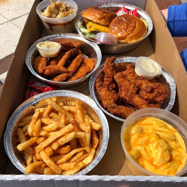 A takeout box filled with burgers, chicken tenders, fries, mac and cheese, and mashed potatoes.